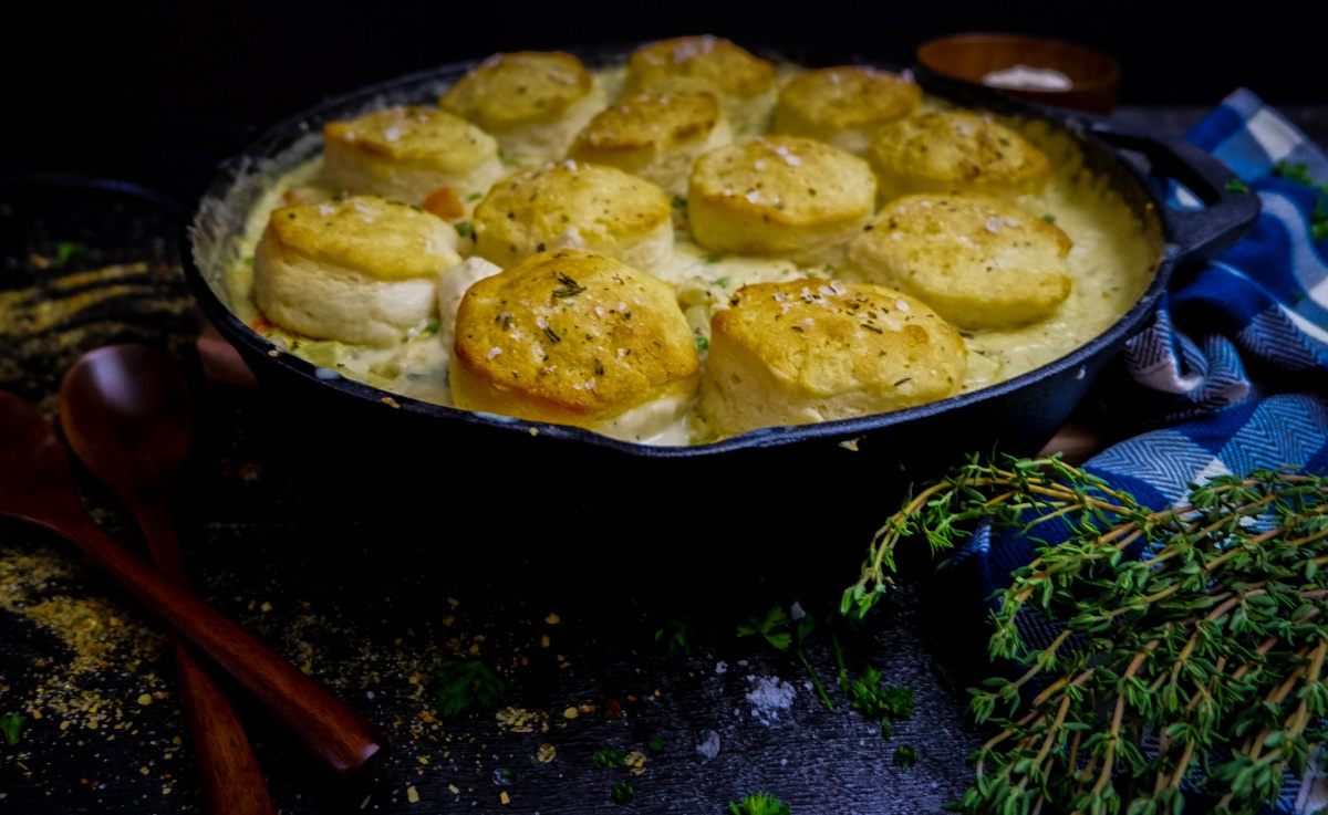 side view of cast iron chicken pot pie with rosemary and two wooden spoons on black table.