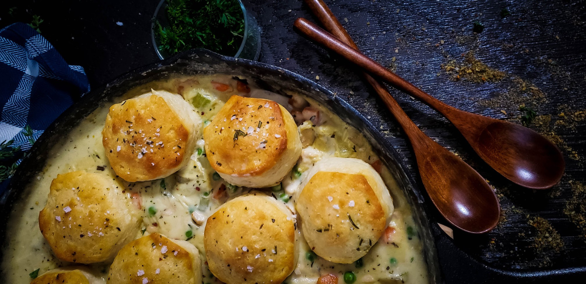 cast iron chicken pot pie with biscuit topping next to two wooden spoons
