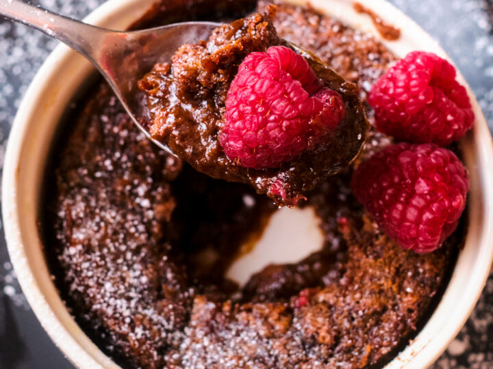 chocolate self saucing pudding in a ramekin with raspberries, showing spoonful of pudding & chocolate sauce