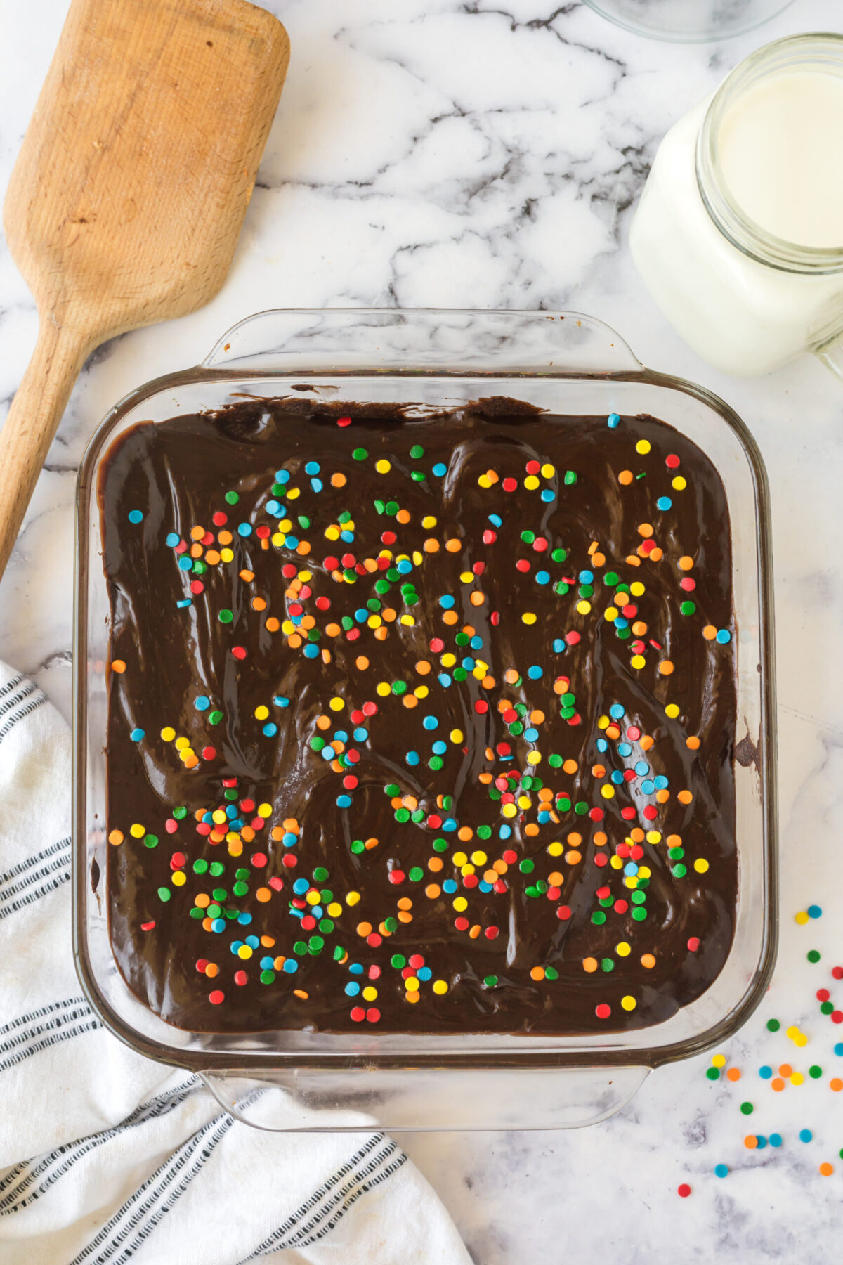 frosted cosmic brownies recipe with rainbow sprinkles in a glass pan
