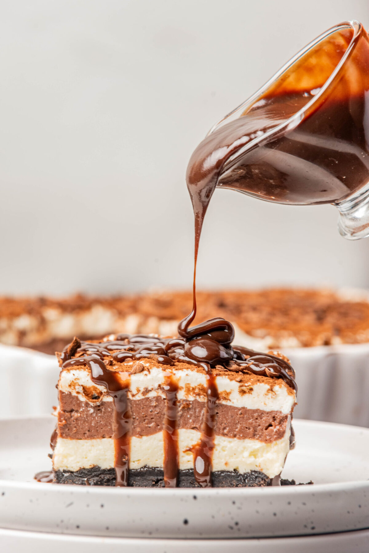 slice of chocolate lasagna recipe on a plate with a chocolate sauce being poured onto it. 