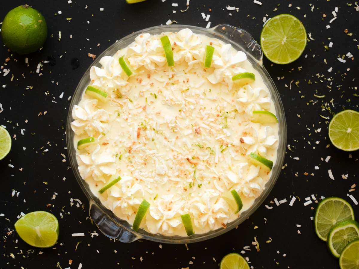 no bake key lime pie whole with lime slices, whipping cream frame and topped with sprinkled toasted coconut