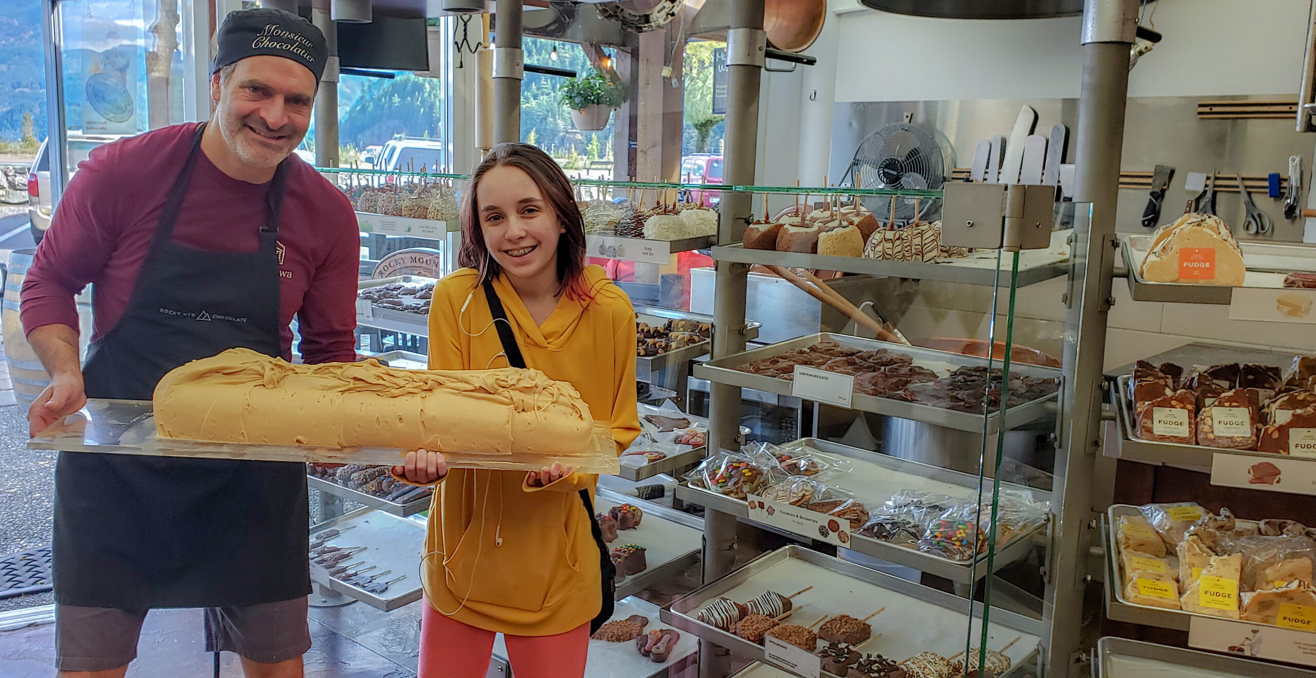 Rocky mountain chocolate store owner and girl holding slab of newly made fudge