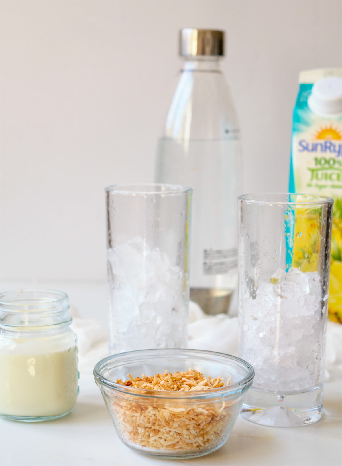 pineapple Italian Soda ingredients glasses with crushed ice, toasted coconut, cream, pineapple juice