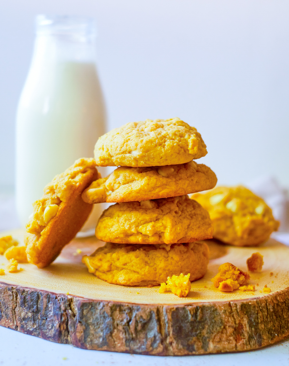 Pumpkin cookies in a stack of 4 with one cookie leaning on stack and jug of milk behind cookies