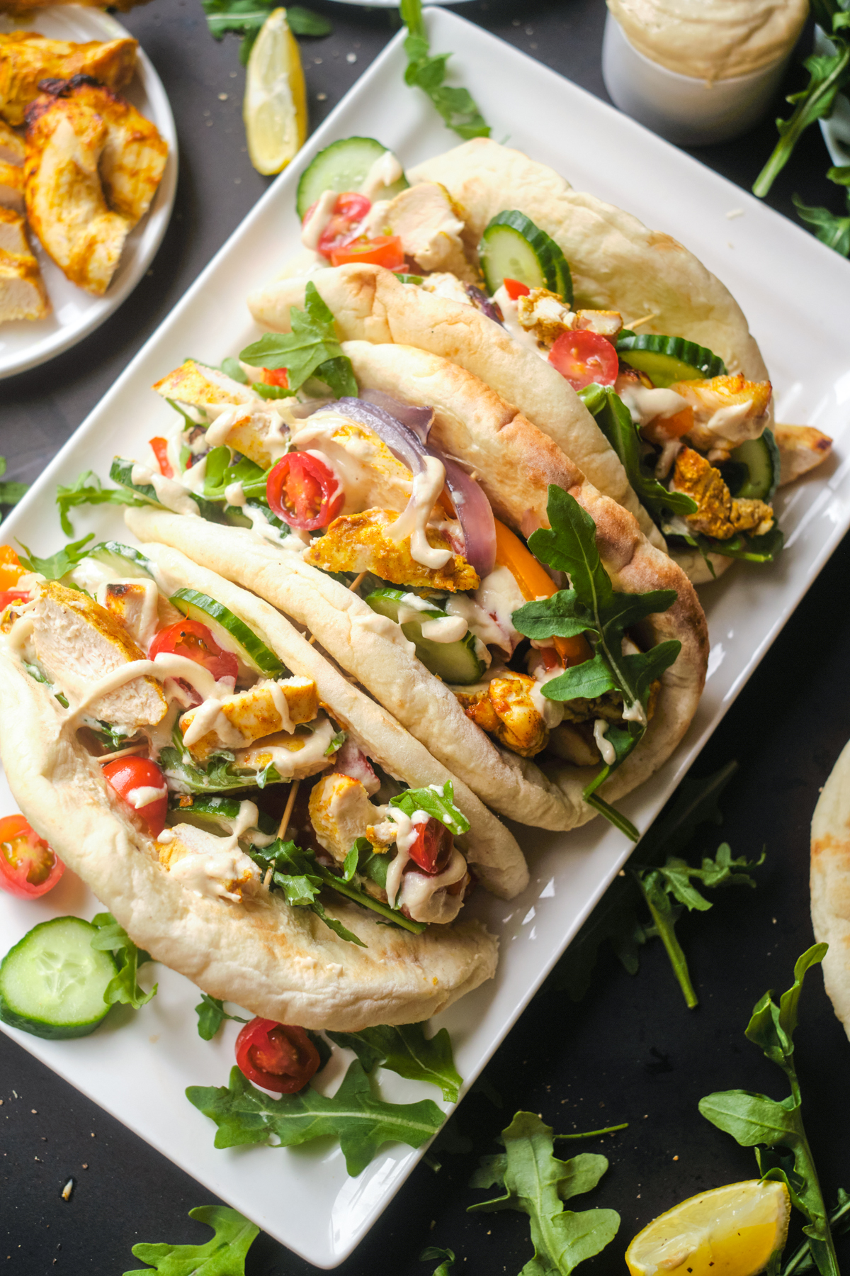 chicken shawarma with tomatoes, cucumber, arugula and topped with tahini sauce in pitas