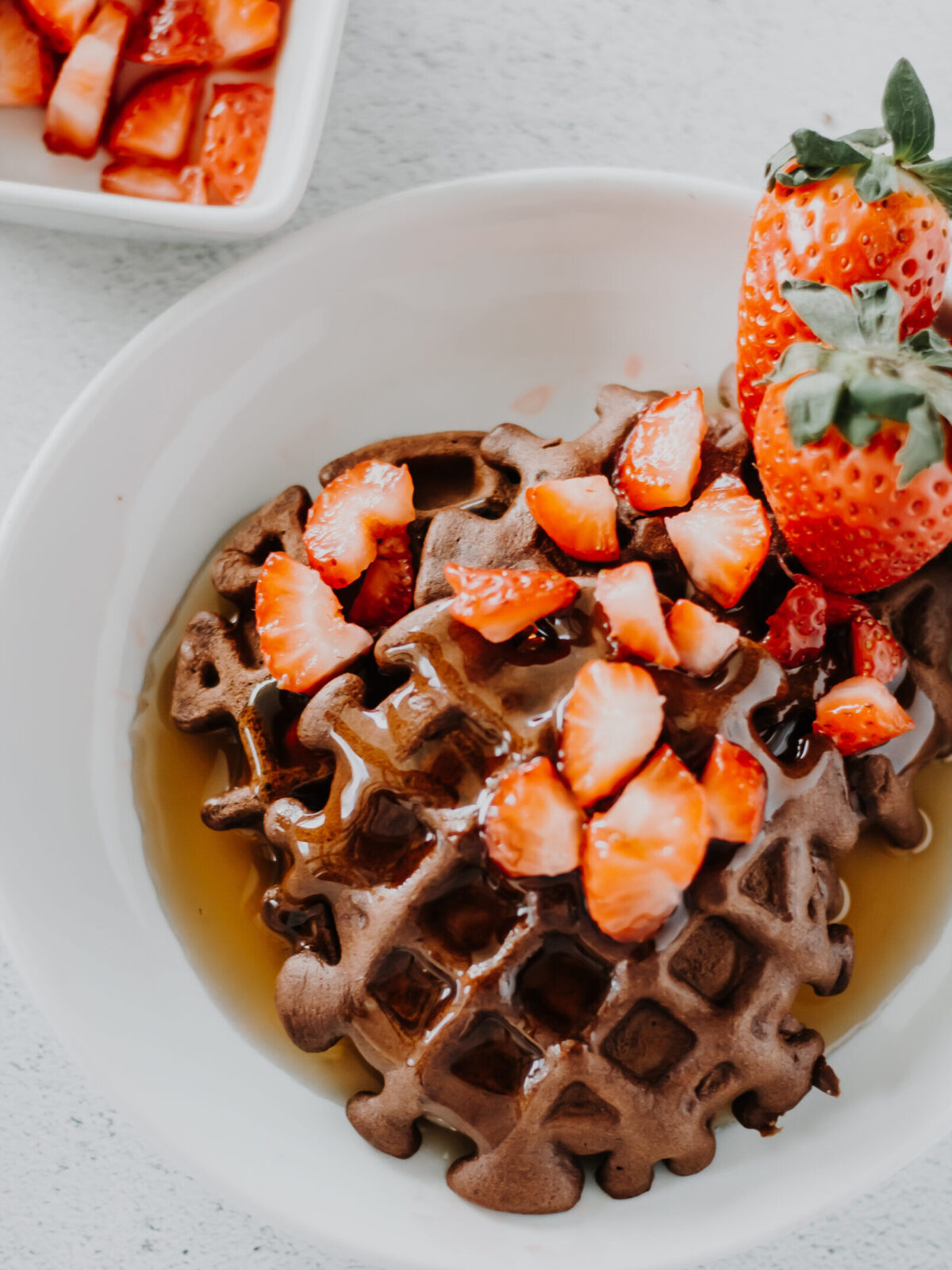 chocolate protein waffle in a shall bowl with strawberries and syrup