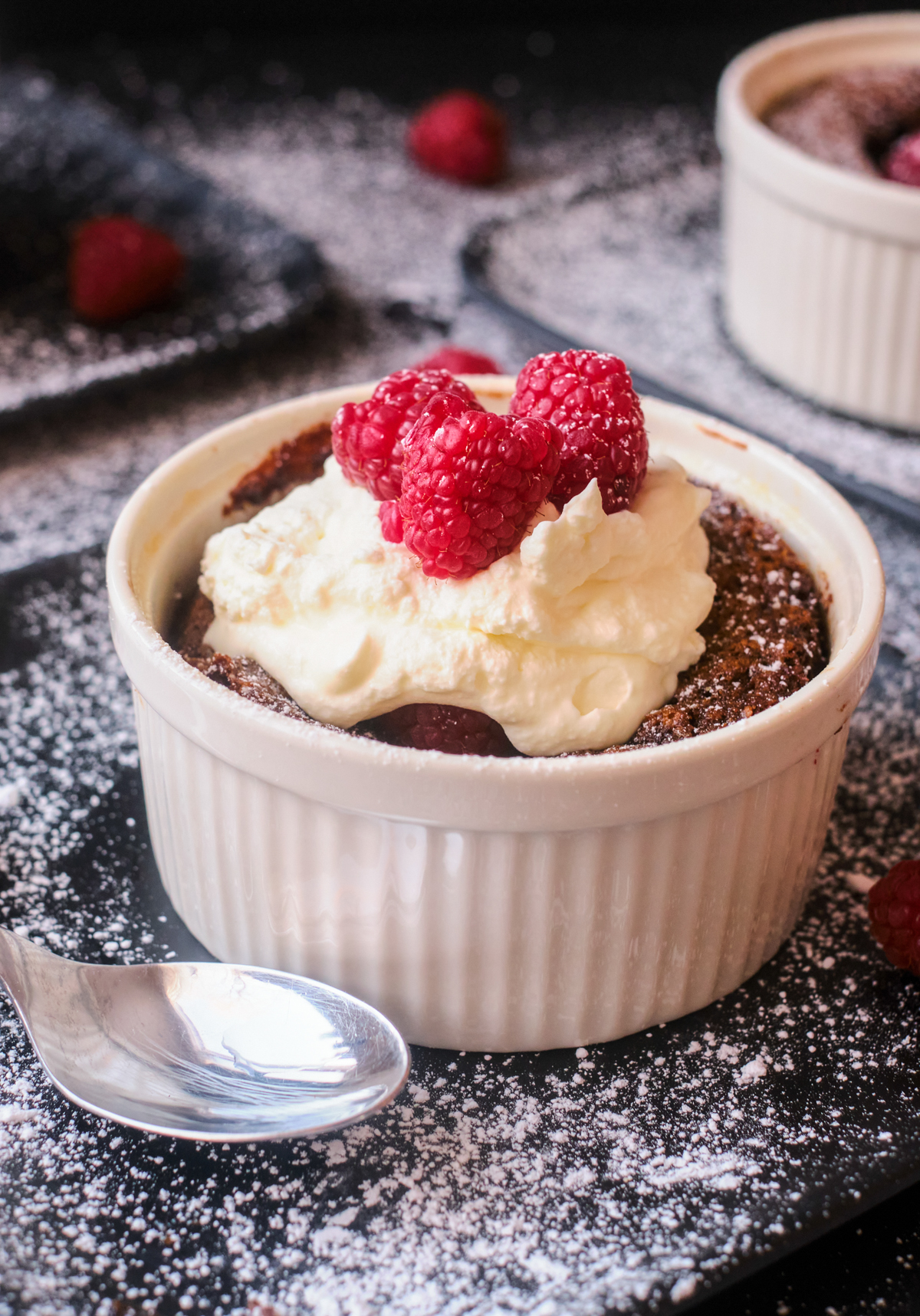 chocolate self saucing pudding in a ramekin with raspberries and whipping cream on top