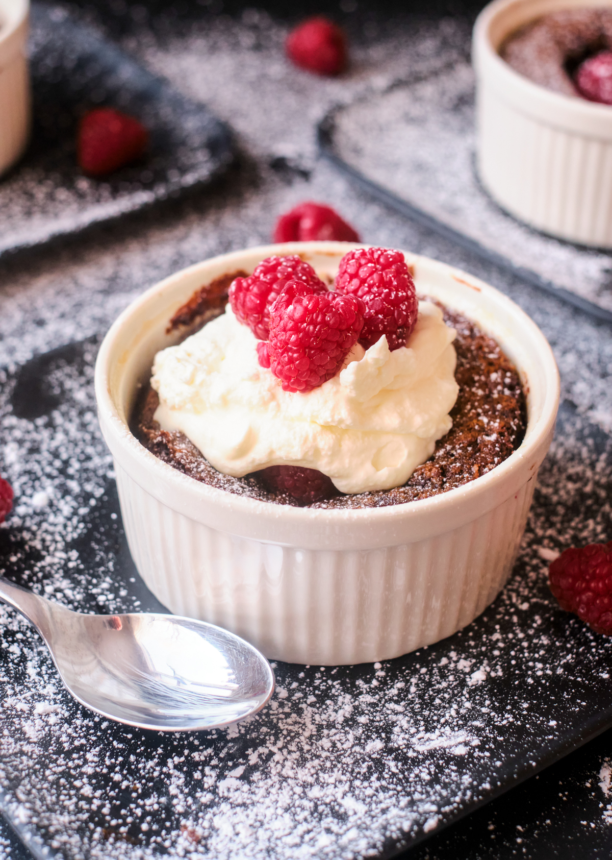 chocolate self saucing pudding recipe in a ramekin with raspberries and whipping cream on top