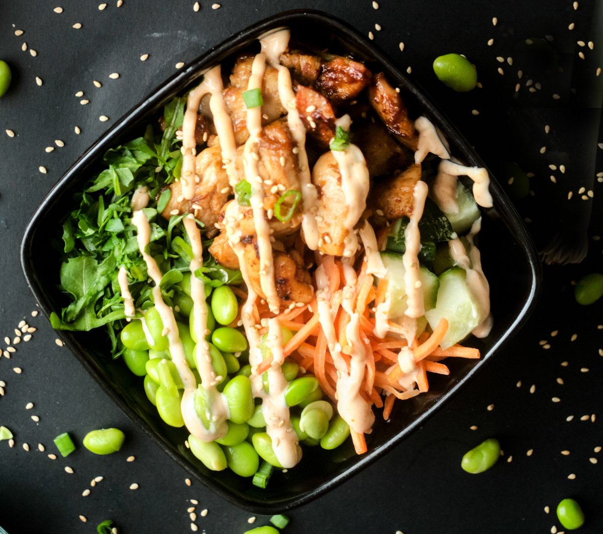 chicken poke bowl made with chicken thighs, edamame, shredded carrots, chopped cucumber and topped with sriracha mayo