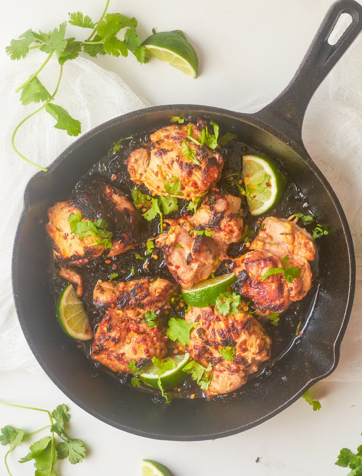 cilantro lime chicken thighs in a cast iron pan with lime wedges