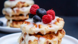 cinnamon roll waffles with blueberries and raspberries on top and cream cheese icing