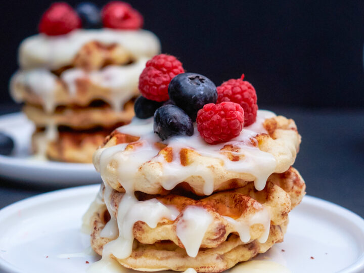 cinnamon roll waffles with blueberries and raspberries on top and cream cheese icing
