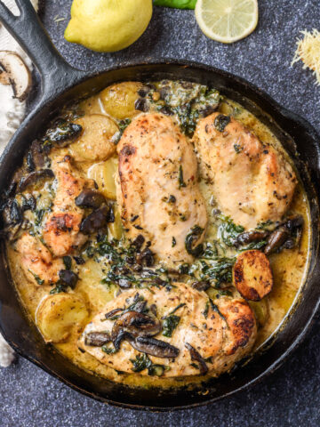 4 chicken breasts, mushrooms, baby potatoes and spinach all cooked in a cast iron pan on a dark background