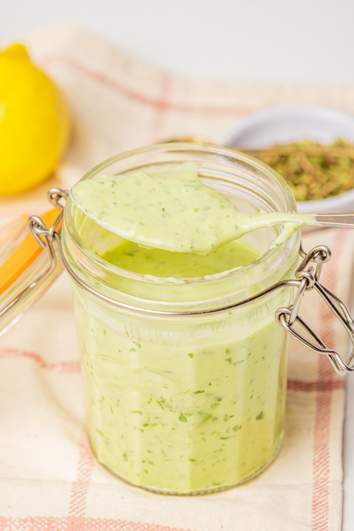 green goddess dressing in a jar with lid and a spoon with some dressing over the jar