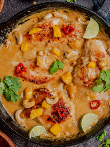 coconut lime chicken in sauce in a cast-iron pan with cilantro and lime wedges